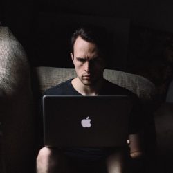 man seating on sofa using MacBook beside window